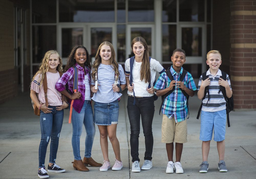 Large Group portrait of pre-adolescent school kids smiling in front of the school building. Back to school photo of a diverse group of children wearing backpacks and ready to go to school
