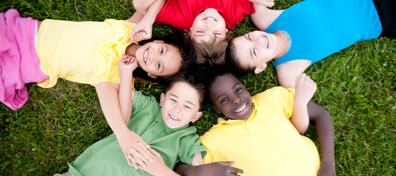 Children laying in the grass in a circle with their arms locked together.